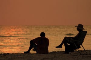 man sits on chair on beach with man sitting on ground outside a licensed detox facility