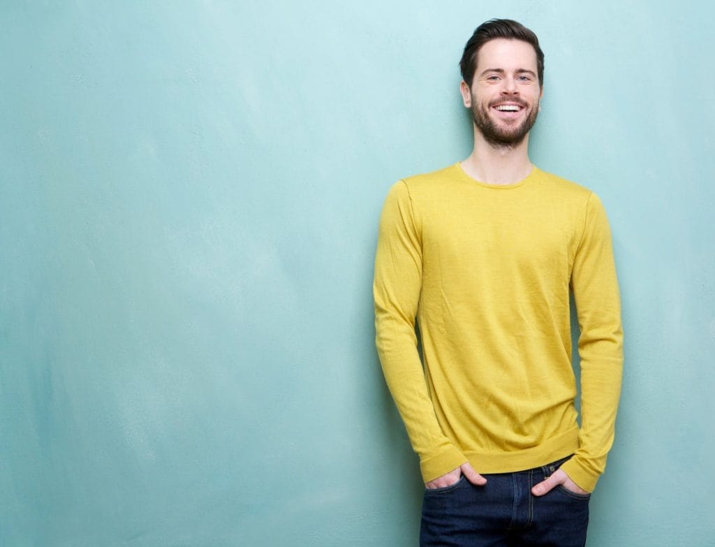 man smiles standing against a blue backdrop discovering what recovery looks like