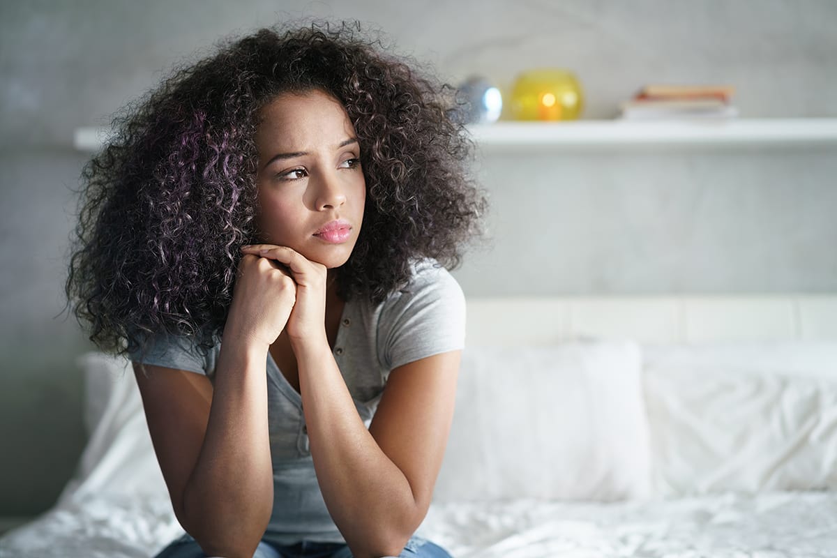 woman sitting on bed dealing with drug withdrawal symptoms