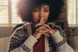 woman with eyes closed and hands on face deep in thought